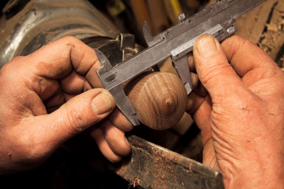 Mains d'artisan mesurant une pièce de bois au pied à coulisse